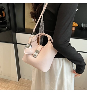 Detalle de bolso tipo cubo rosa claro con colgante de corazón y hebilla de metal en la correa