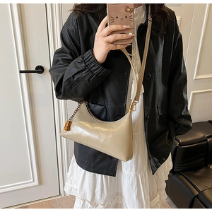 Detail einer beigen glänzenden Hobo-Tasche mit goldener Kette und schmalem Schultergurt
