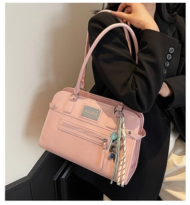 Detail view of pink PU leather shoulder bag featuring a metal plate and fringe tassel