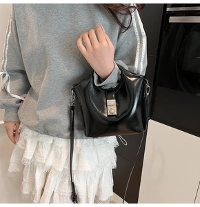 Detail view of black glossy bucket bag featuring elegant pearl lock and silver buckle
