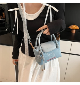 Detail of light blue denim dumpling bag featuring cartoon embroidery and a dog charm