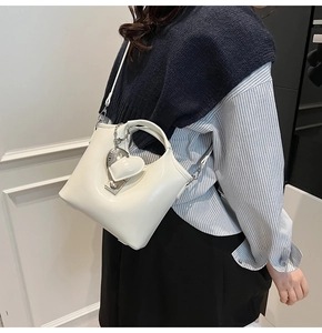 Detail of a white bucket bag with silver heart charm and crossbody strap for women