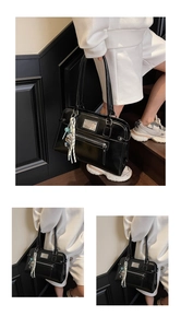Detail of black leather tote bag with silver plate, zipper pocket and bear charm accessory