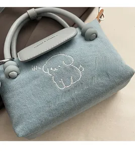 Detail of light blue denim bag featuring white dog embroidery and gray leather handle
