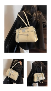 Detail view of cream-colored shoulder bag with metal logo, zipper pocket and tassel charm