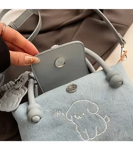 Detail of light blue denim crossbody bag with magnetic buckle and dog embroidery
