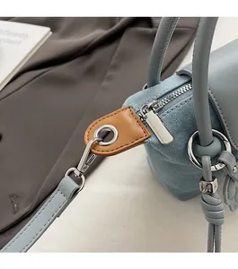 Close-up of denim shoulder bag with silver zipper and letter M metal pendant detail