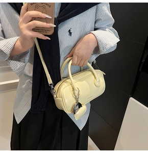 Detail of a creamy yellow glossy handbag featuring dual handles and heart charm