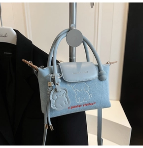 Detail of light blue denim bag with dog embroidery, leather handle and pendant