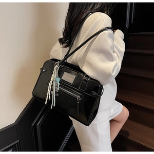 Detail of glossy black leather shoulder bag featuring a metal logo and teddy bear charm