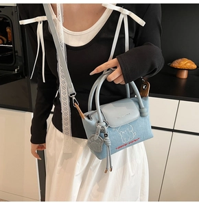 Detail of light blue denim crossbody bag featuring cartoon puppy print and leather handle