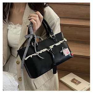 Detail of black faux leather handbag featuring white lace trim and a plaid ribbon bow