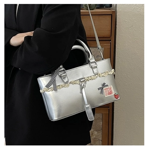 Detail of silver handbag with lace trim, bow, and strawberry charm worn by a model