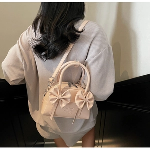 Détail d'un sac Boston rose clair avec nœuds porté en bandoulière sur le mannequin