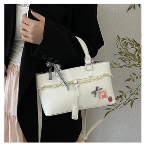 Detail of white PU leather handbag featuring lace edges, a bow, and a strawberry charm