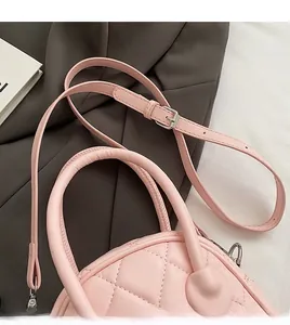 Detail of light pink quilted handbag featuring an adjustable shoulder strap and leather handle