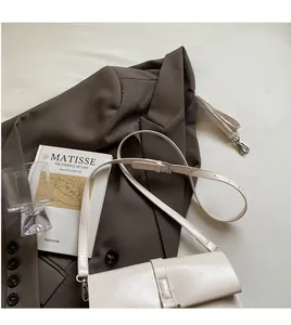 Detail view of cream-white vintage shoulder bag on a blazer with artistic accessories