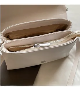Detail of minimalist cream leather bag showing dual compartments and smooth zipper