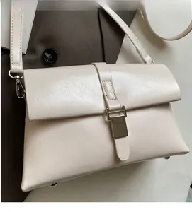 Macro detail of creamy faux leather texture and rectangular metal buckle on a shoulder bag