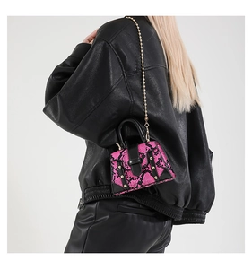 Nahaufnahme der rosa Schlangenhaut-Minitasche mit Goldkette auf schwarzer Lederjacke