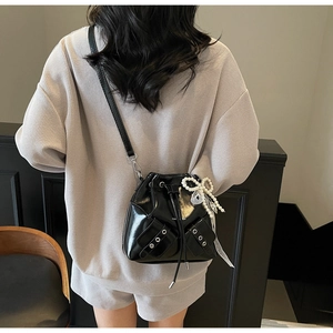 Détail du sac seau en cuir verni noir avec poches à œillets et nœud en perles