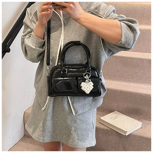 Detail einer schwarzen Lackleder-Boston-Tasche mit Perlenherz-Anhänger und kleinen Fronttaschen