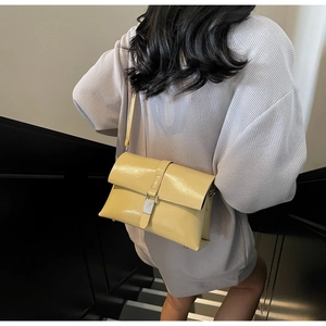 Detail view of pale yellow patent leather shoulder bag with metallic silver buckle closure