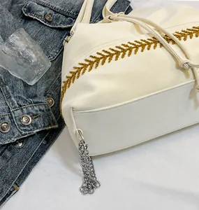 Dettaglio della borsa in pelle bianca con ricamo marrone e ciondolo a catena in metallo