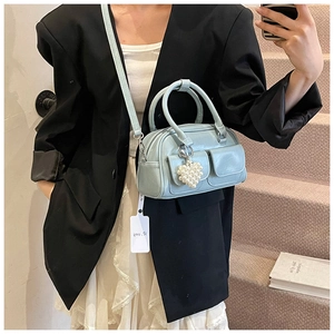 Detail of light blue Boston bag featuring heart pearl charm and front flap pockets