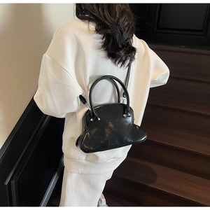 Polished black shell bag shown on a model against wooden stairs background