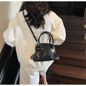 Glossy black shell-shaped handbag with adjustable strap shown on a model on stairs