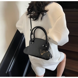 Glossy black shell-shaped leather bag styled as crossbody on white casual wear