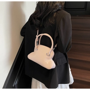 Pink glossy shell bag with round handles worn by a model in a black suit over stairs