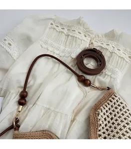Detail of woven straw shoulder bag with brown leather strap and wooden bead accents