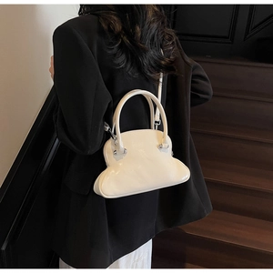 Close-up of cream shell handbag with glossy finish on a dark suit background