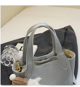 Close-up of gray lychee pattern leather bucket bag with gold hardware and plush charm