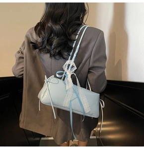 Back view of light blue underarm bag with white lace and ribbon on a grey suit