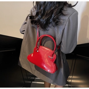 Detail of glossy red shell bag with silver hardware on model in grey suit blazer