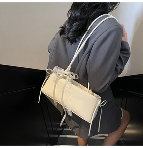 Detailed view of white patent leather baguette bag with lace bows on model shoulder