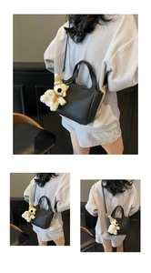 Detail of black litchi grain leather bucket bag with white plush bear charm and strap