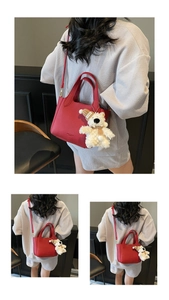 Detail of red lychee leather handbag with brand logo and cute plush bear charm