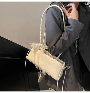 Detail of cream shoulder bag featuring elegant lace bow and satin ribbon strap accent