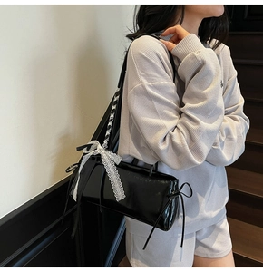 Detail of black glossy shoulder bag with white lace bow and ribbons on interior stairs