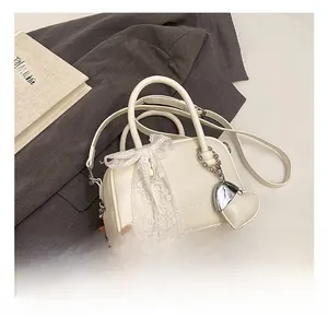 Détails d'un sac à main blanc avec nœud en dentelle et pendentif en métal en forme de cœur