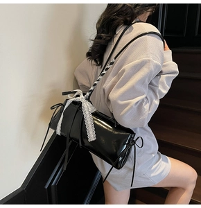 Close-up of black glossy shoulder bag with white lace bow detail on a leather surface