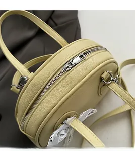 Detail view of beige lychee leather bowling bag with silver zipper and printed ribbon