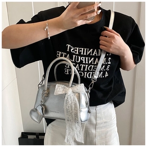 Détail du sac Boston argenté avec un nœud en dentelle blanche et un pendentif cœur