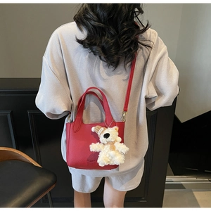 Detail of red lychee leather bucket bag with cute teddy bear charm on model back