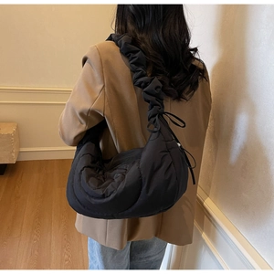 Detail of a black quilted puffer hobo bag featuring a ruffled shoulder strap with a bow