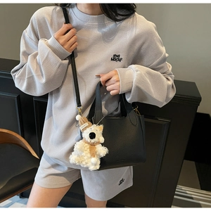 Detail of black lychee grain leather bucket bag with a cute plush bear charm accessory